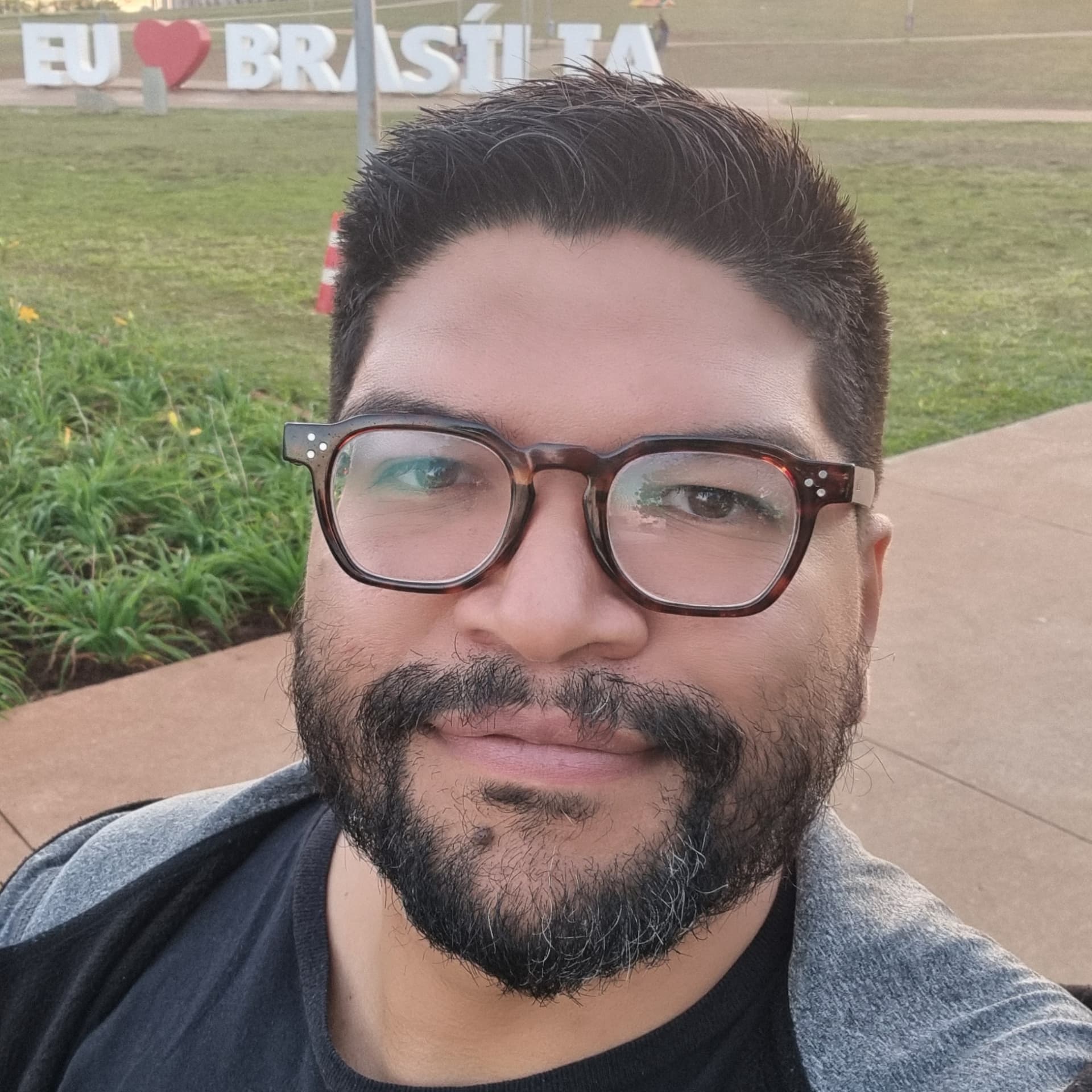 Marcio Pereira Vidal sorrindo em frente à placa Eu Amo Brasília
